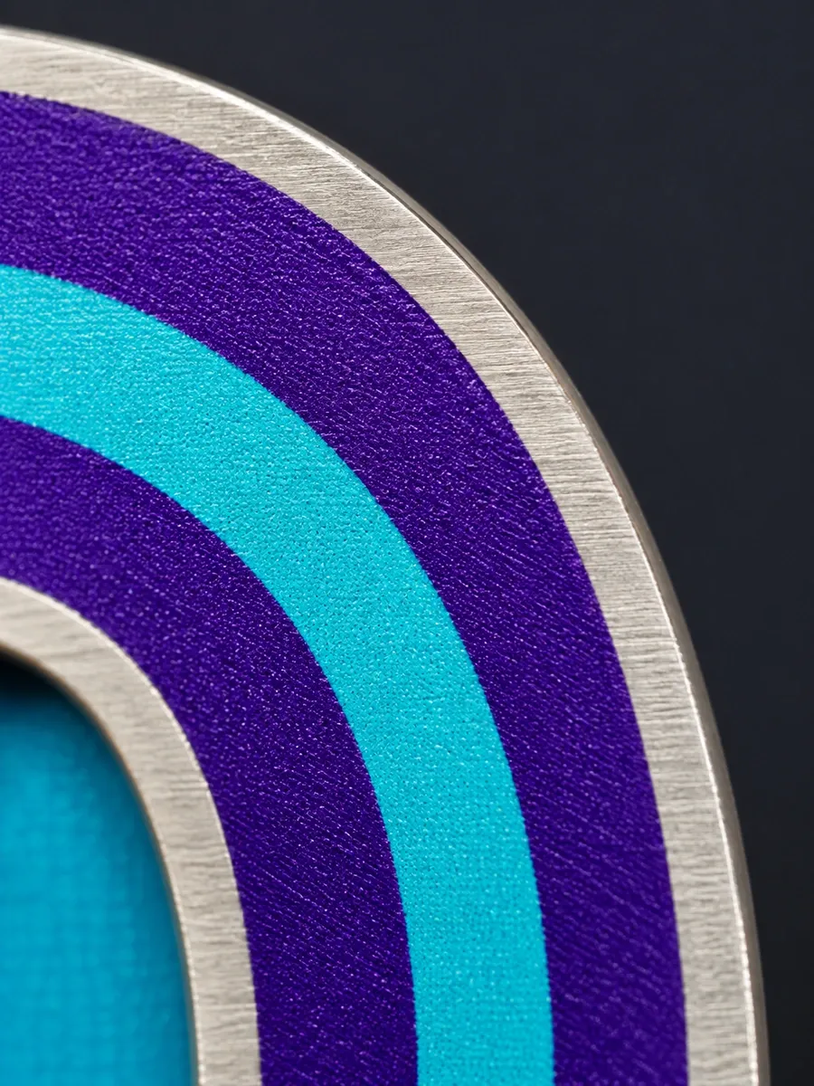 Macro of UV print on steel: purple and turquoise bands framed by brushed metal